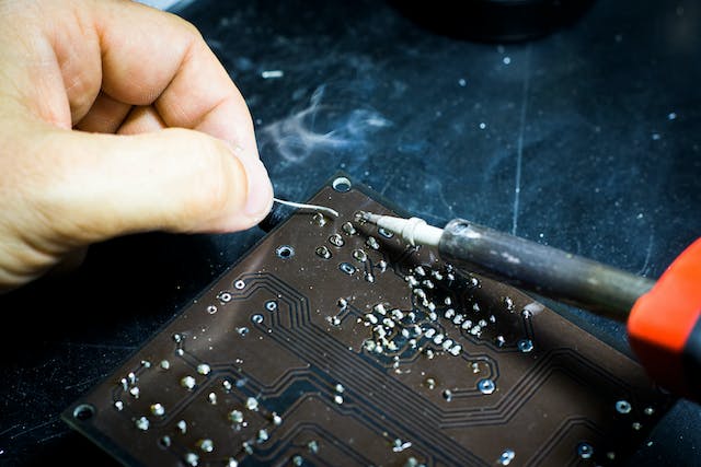 A person using a soldering iron on a device board. 