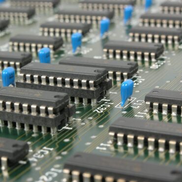 Close-up view of an electronic circuit board with multiple black integrated circuits and blue capacitors.