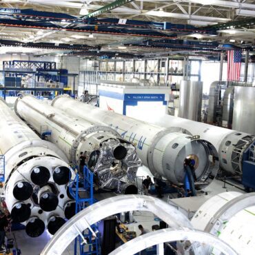Aerospace manufacturing facility with multiple rocket stages on the factory floor during assembly and processing.