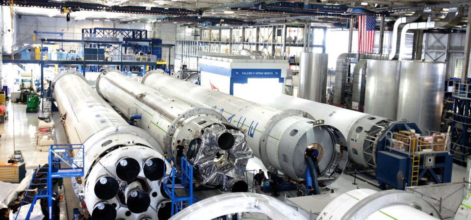Aerospace manufacturing facility with multiple rocket stages on the factory floor during assembly and processing.