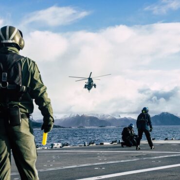 Military crew guides a helicopter on a naval flight deck