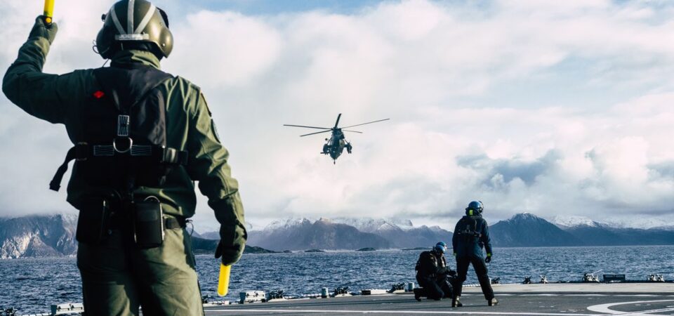 Military crew guides a helicopter on a naval flight deck
